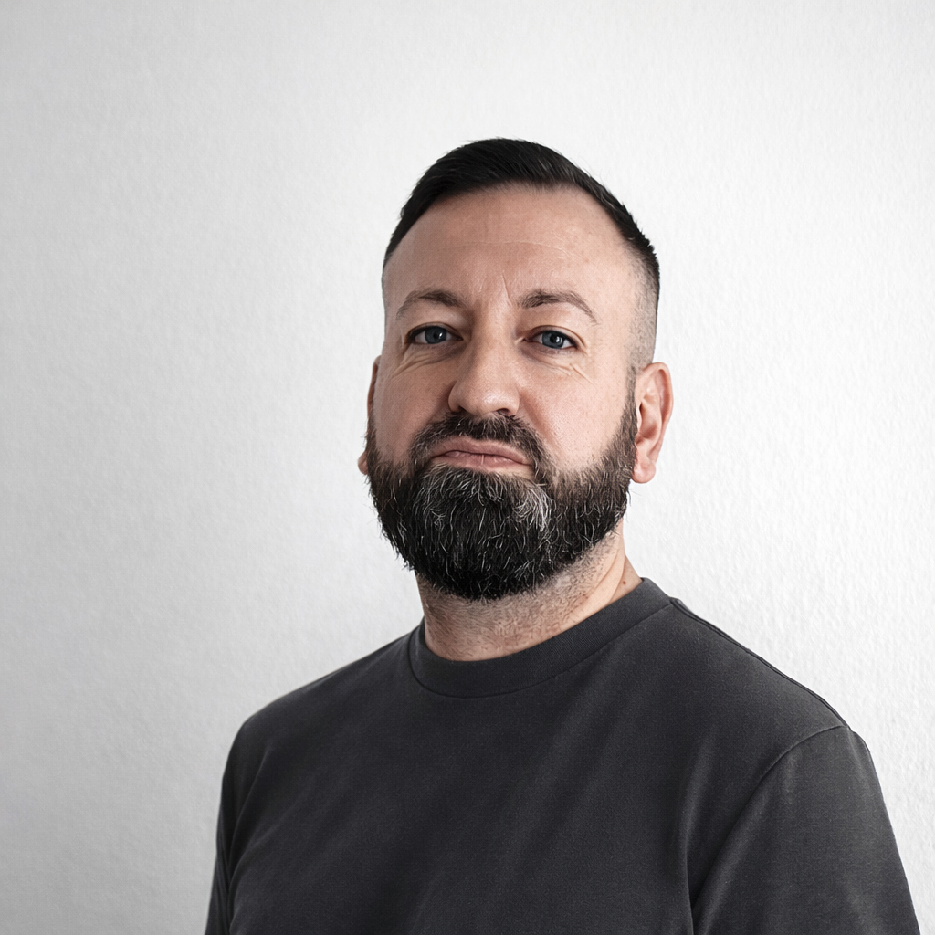 Studio-Porträt eines bärtigen Mannes mit kurzen Haaren vor grauem Hintergrund